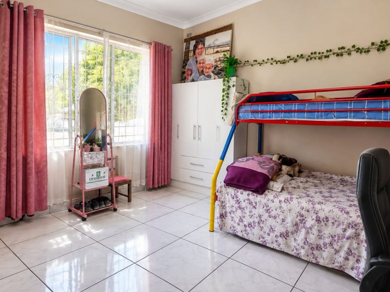 A well-lit bedroom featuring tiled flooring, a built-in wardrobe, and large windows with security bars, offering a functional and comfortable living space.
