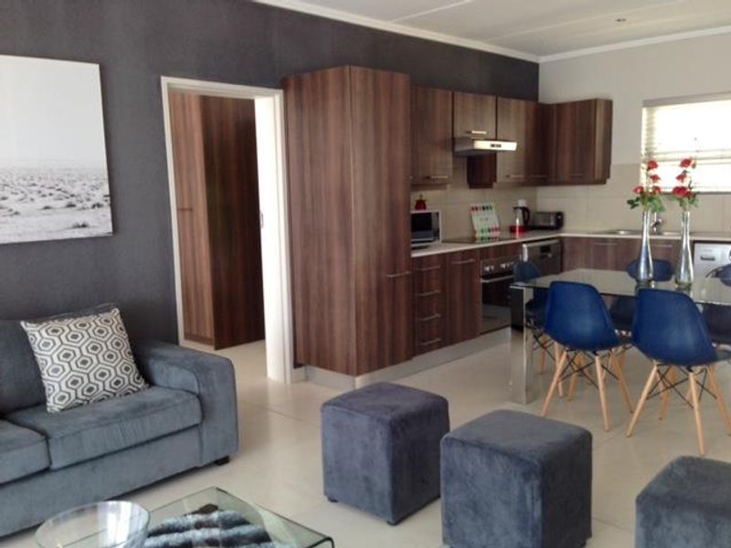 Open-plan living and kitchen area featuring modern wood-finish cabinetry, integrated appliances, and neutral tiled flooring, creating a functional and cohesive living space.