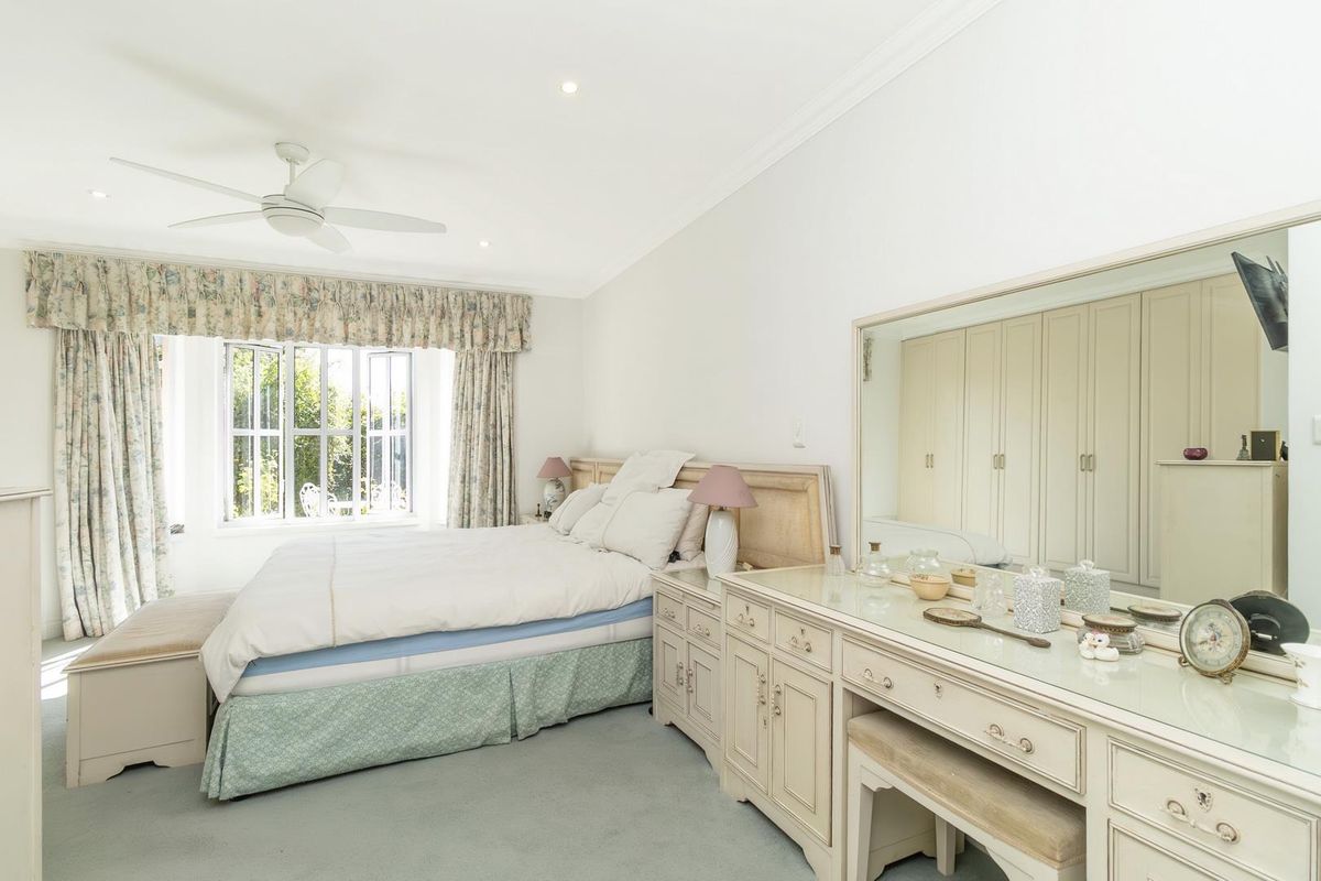 A well-lit bedroom featuring built-in wardrobes, a ceiling fan, and large windows with garden views.