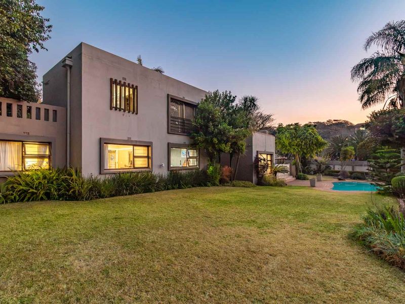 Rear view of the property featuring a well-maintained garden, paved patio area, and a swimming pool set against the building facade.
