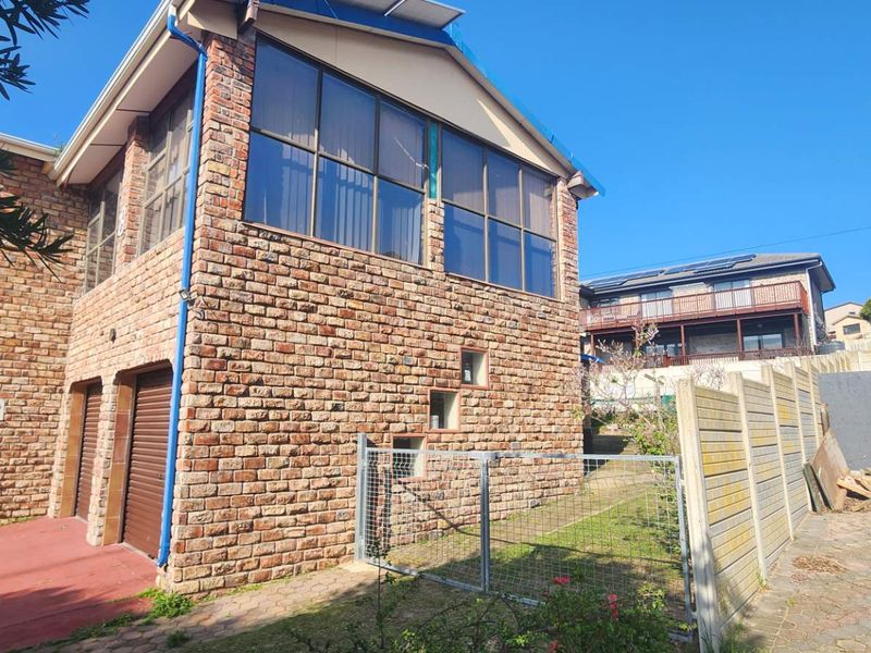 Rear view of a double-story face brick house featuring large windows, integrated garage doors, and a paved outdoor area with boundary walling.