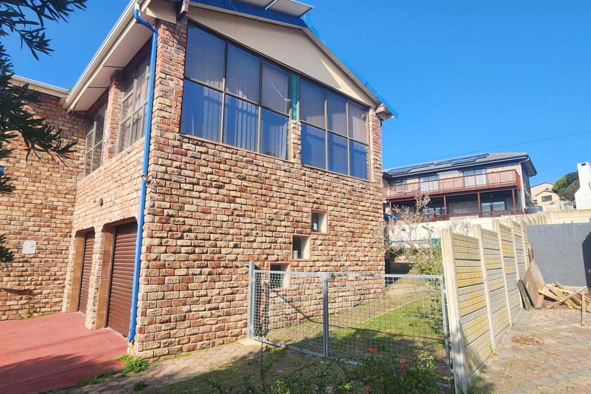 Rear view of a double-story face brick house featuring large windows, integrated garage doors, and a paved outdoor area with boundary walling.