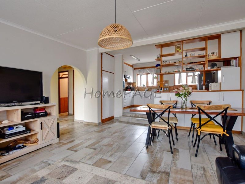 Open-plan living and dining area featuring tiled floors, an arched entryway, and a functional kitchen with built-in cabinetry and open shelving.