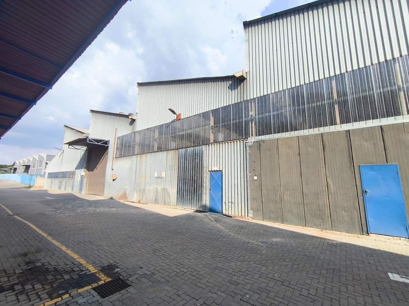 Exterior view of an industrial warehouse facility featuring corrugated metal cladding, paved access area, and multiple steel entry points.