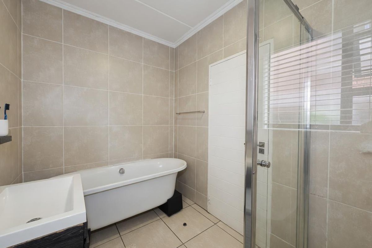 Modern bathroom featuring a freestanding bathtub, a separate glass-enclosed shower, and neutral floor-to-ceiling wall tiling.