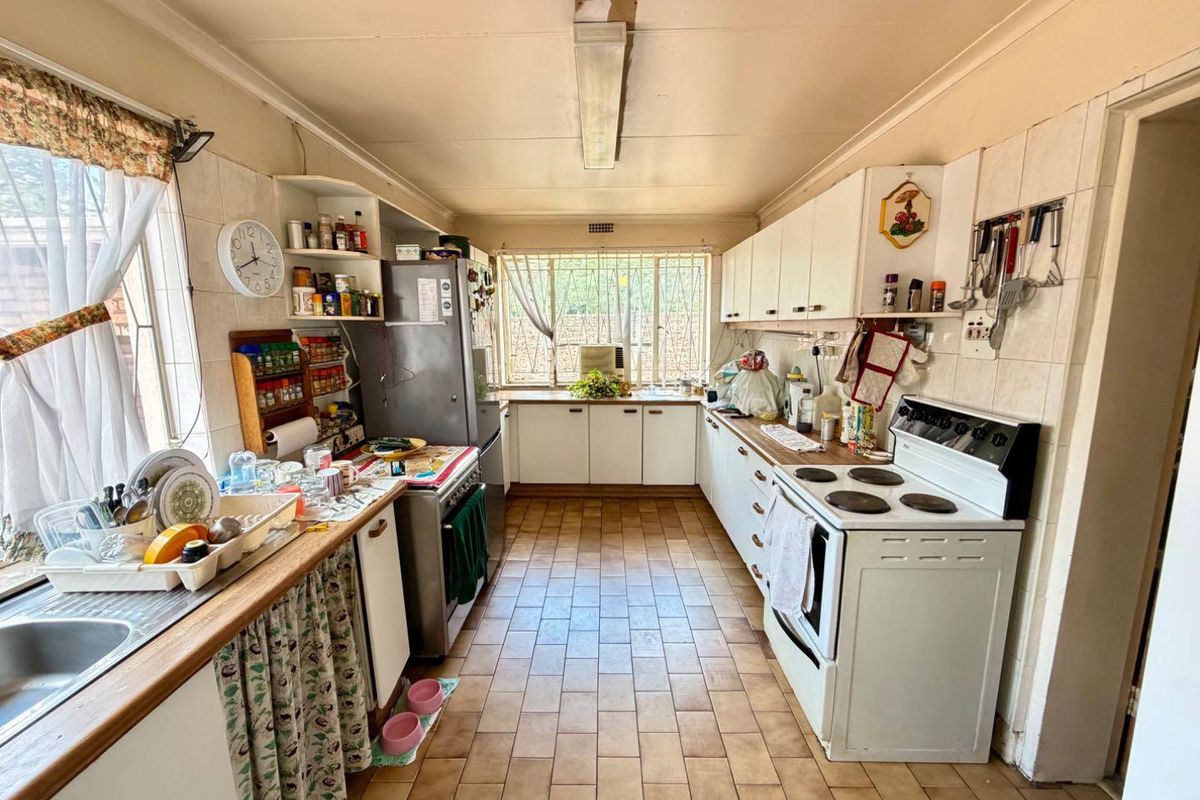 A dated kitchen featuring original cabinetry, tiled flooring, and a functional layout with built-in stove and sink area, ready for modernization.