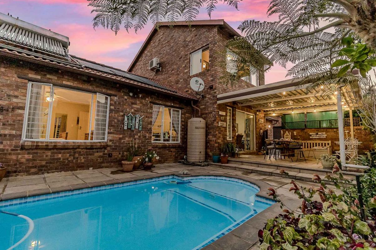 Rear exterior view of a brick townhouse featuring a swimming pool, covered patio area, and integrated solar water heating system.