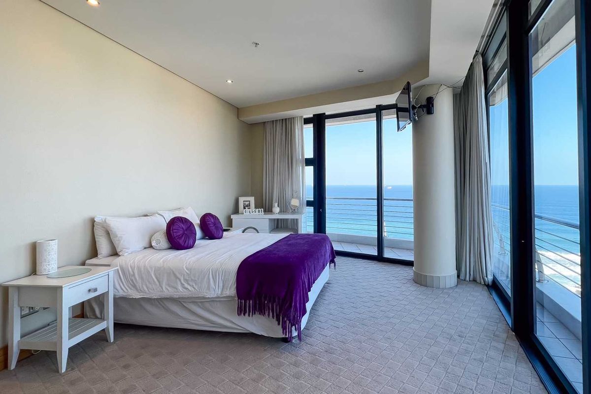 Spacious bedroom featuring floor-to-ceiling glass sliding doors that open onto a private balcony with expansive ocean views.