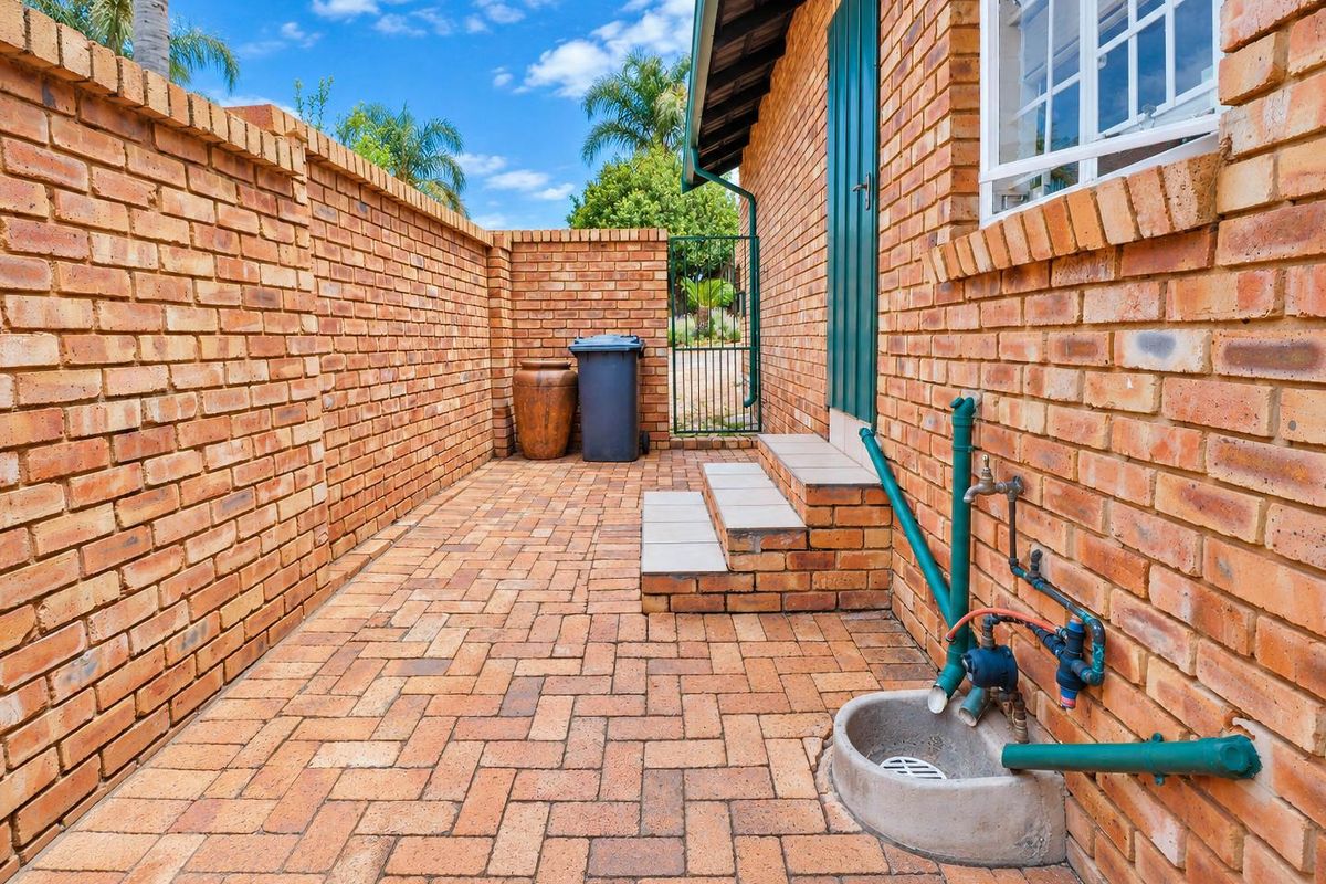 A private rear courtyard featuring brick walling, paved flooring, and external utility access with a drainage gully and water connection.
