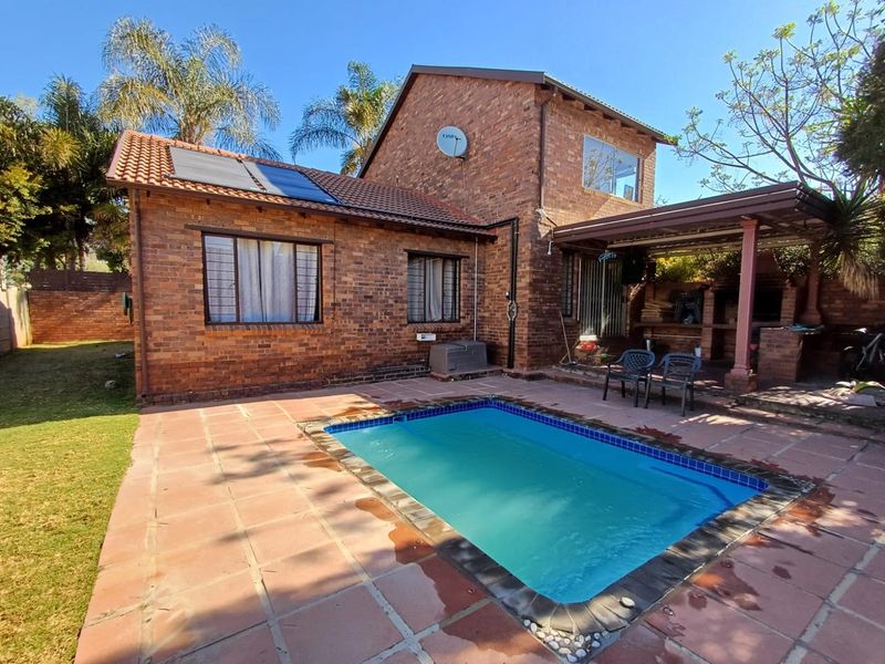 Rear exterior view of a brick townhouse featuring a swimming pool, solar water heating panels, and a covered patio area with a built-in braai.