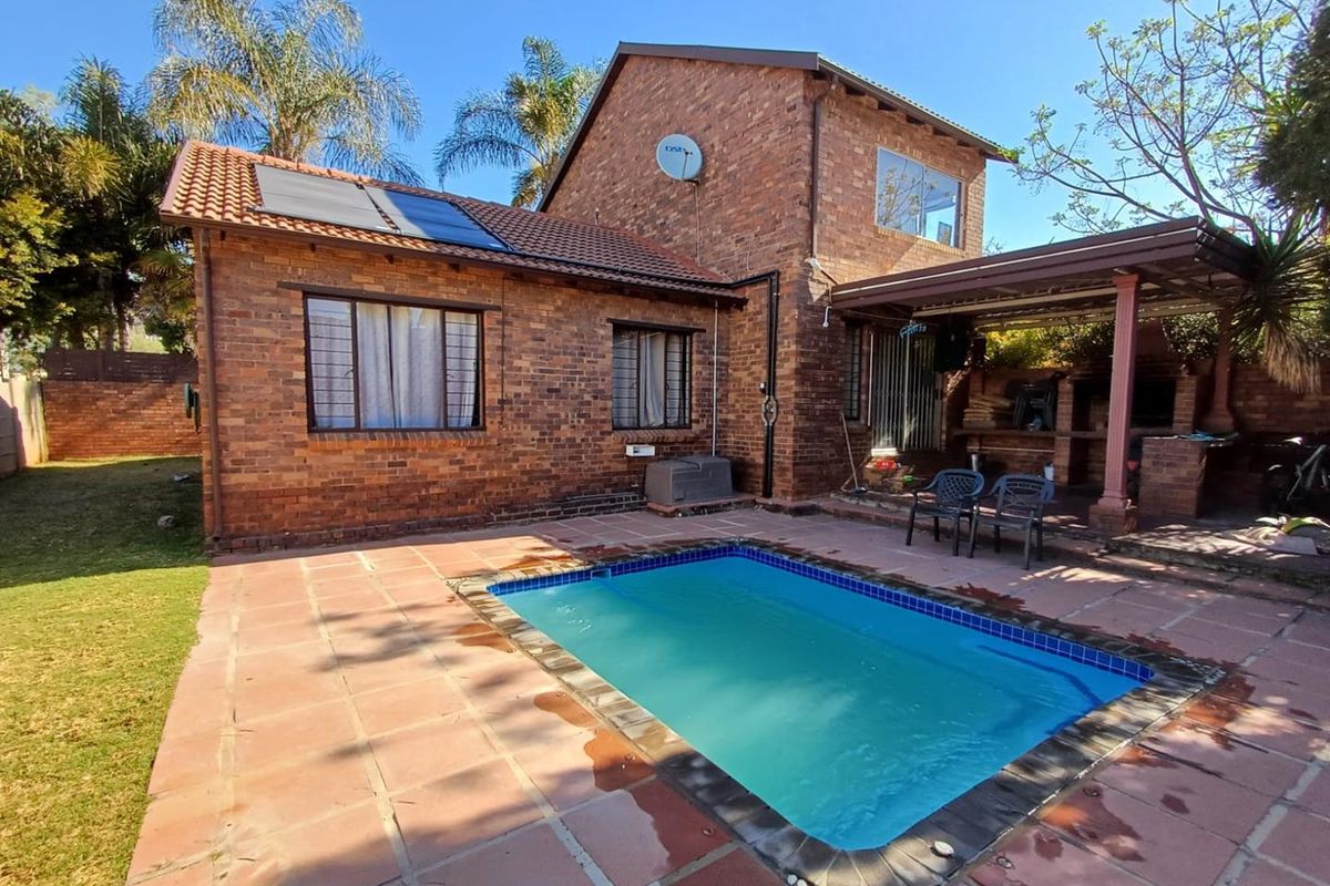 Rear exterior view of a brick townhouse featuring a swimming pool, solar water heating panels, and a covered patio area with a built-in braai.