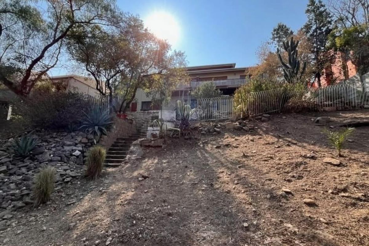 Rear view of the property featuring a sloped garden, stone retaining walls, concrete stairs, and a balcony overlooking the outdoor space.