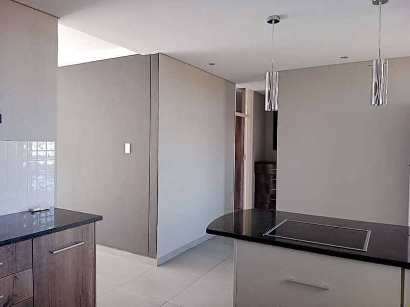 Modern kitchen featuring a central island with a built-in hob, granite countertops, sleek cabinetry, and contemporary pendant lighting in an open-plan layout.