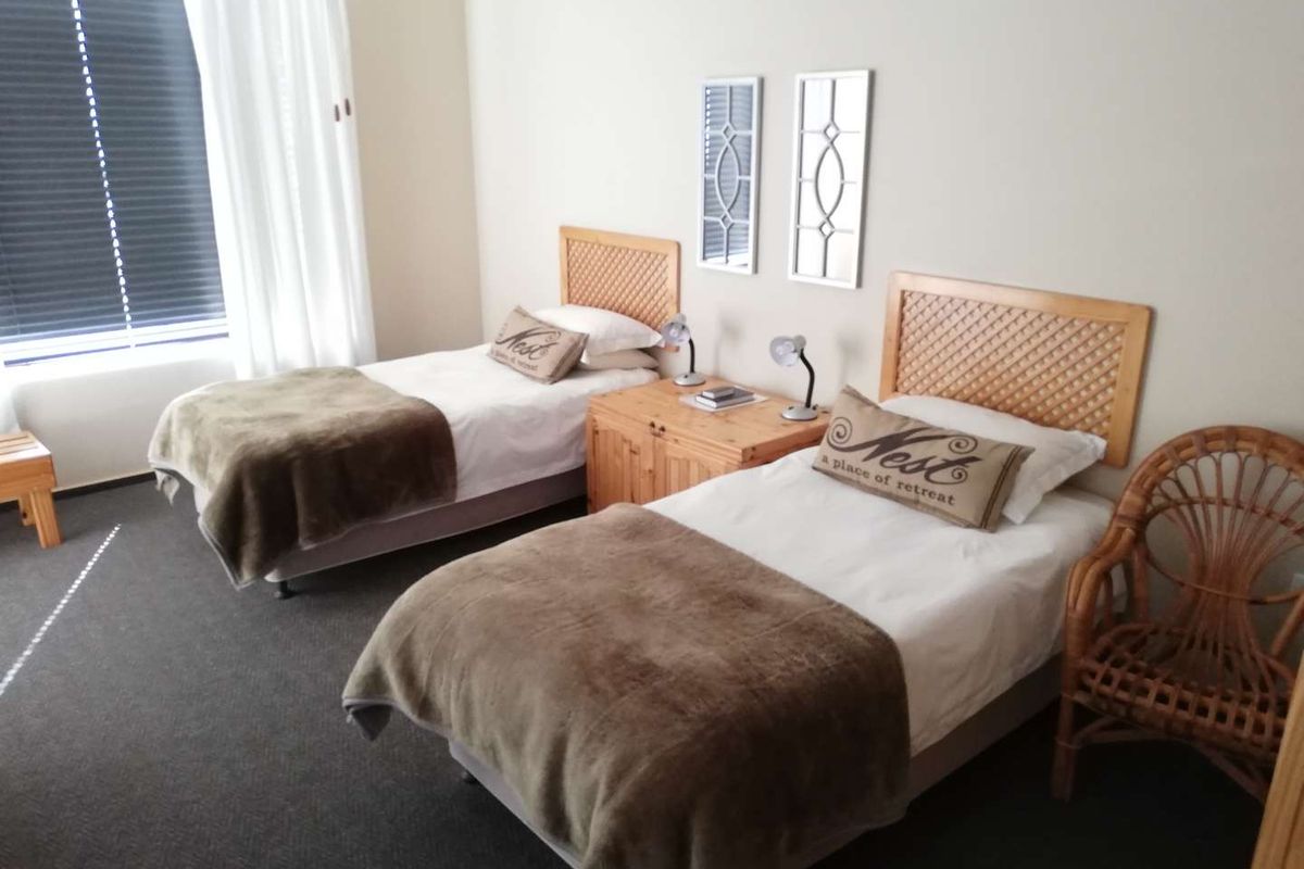A bedroom featuring two single beds with wooden headboards and a central bedside table, finished with neutral wall tones and carpeted flooring.