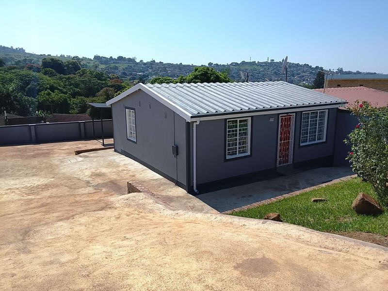 A detached single-story house featuring a corrugated metal roof, security bars on windows, and a paved driveway area with surrounding perimeter walling.