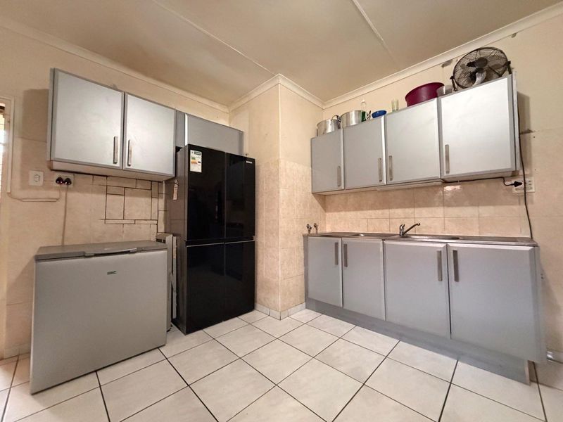 A functional kitchen featuring built-in cabinetry, tiled flooring, and a tiled backsplash, offering a practical layout for daily food preparation.