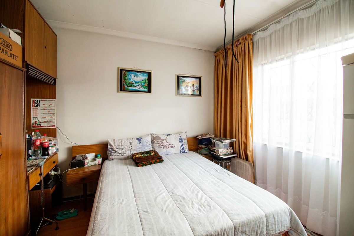A compact bedroom featuring built-in wooden cabinetry, a large window with curtains, and laminate flooring.