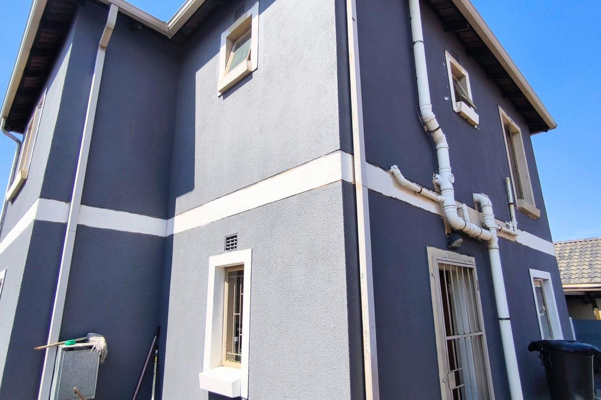 A view of the side exterior elevation of a two-story house featuring dark grey textured walls with white trim and visible drainage infrastructure.