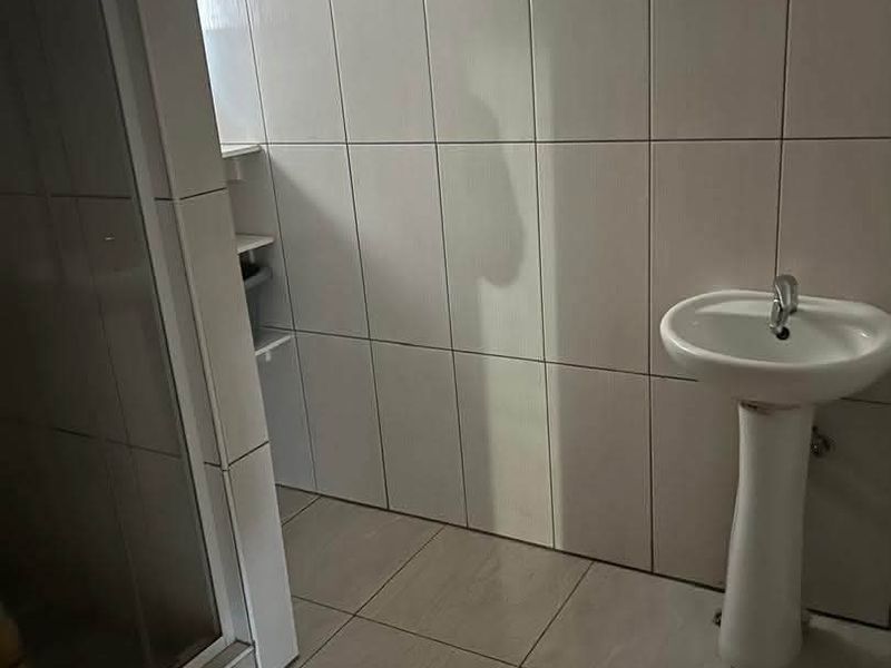 A functional bathroom featuring a pedestal basin and a glass-enclosed shower, finished with neutral wall and floor tiling.
