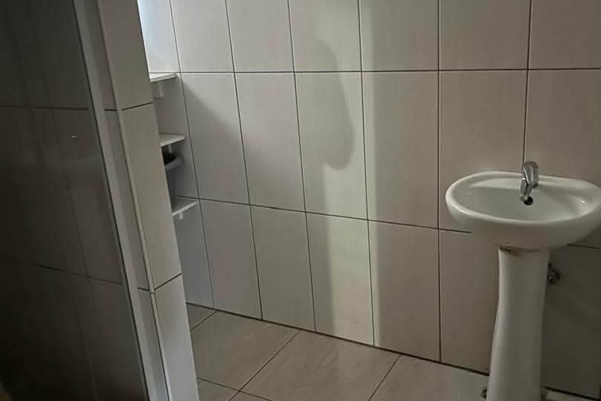 A functional bathroom featuring a pedestal basin and a glass-enclosed shower, finished with neutral wall and floor tiling.
