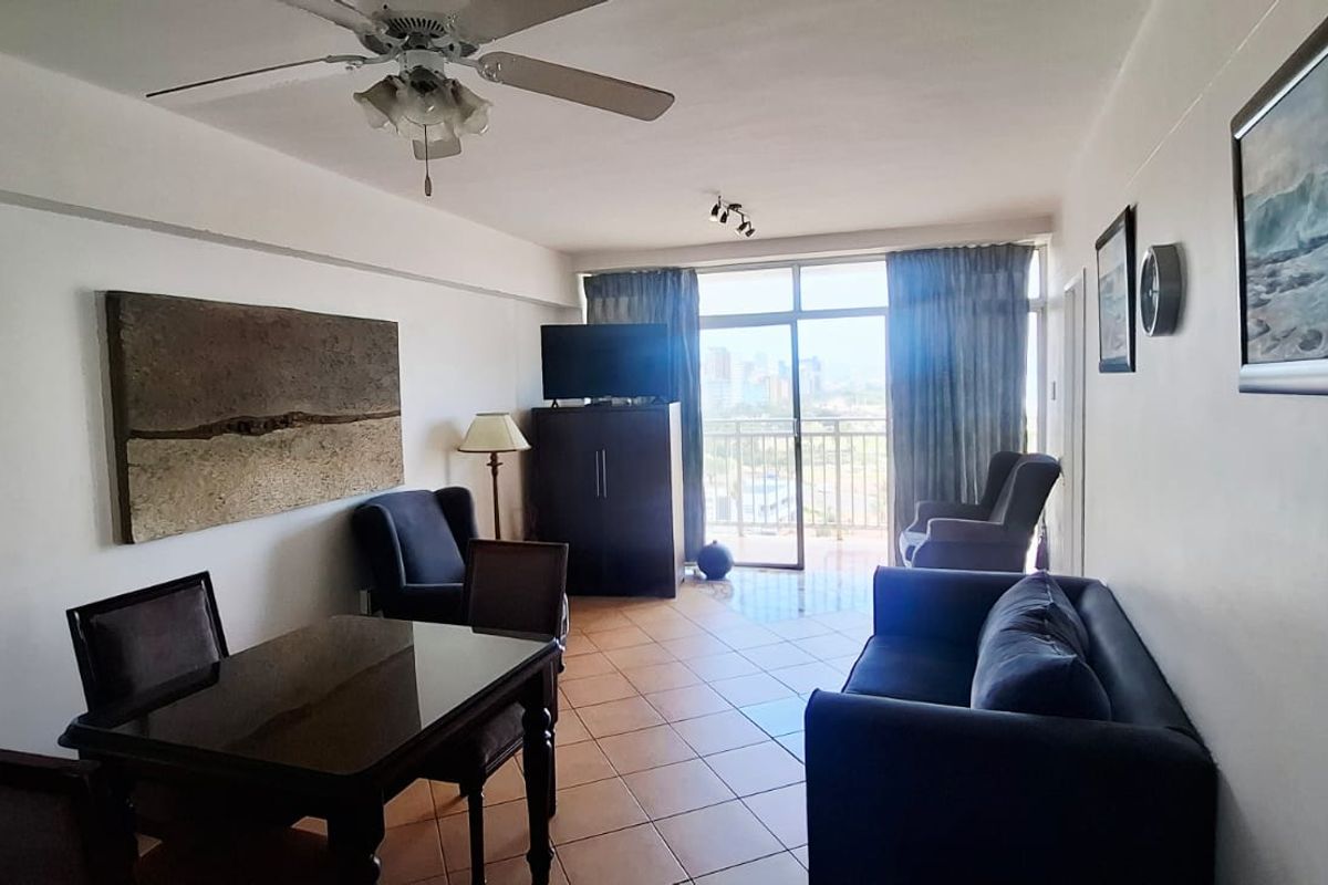 A living and dining area featuring tiled flooring, a ceiling fan, and large sliding glass doors leading to a balcony with city views.