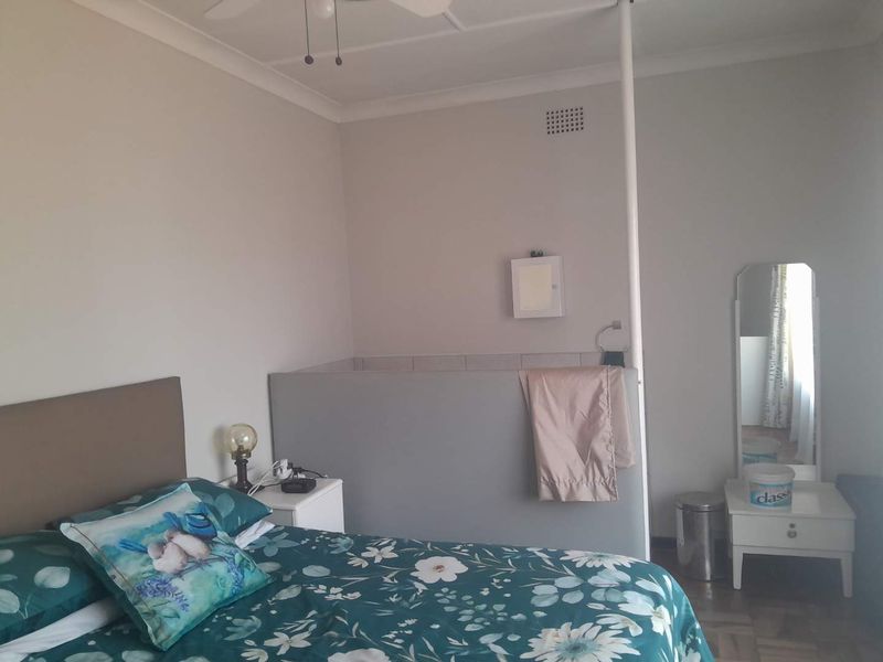 A bedroom featuring a partition wall, ceiling fan, and ventilation grille, offering a functional layout with neutral wall finishes.