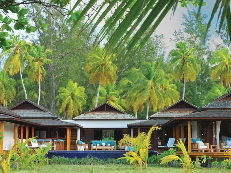 A luxurious villa exterior featuring a private swimming pool, expansive timber decking, and traditional pitched roof architecture set against a lush tropical garden.