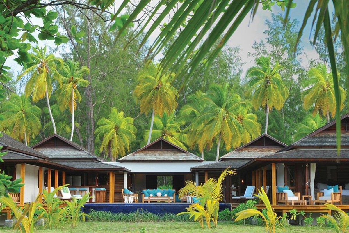 A luxurious villa exterior featuring a private swimming pool, expansive timber decking, and traditional pitched roof architecture set against a lush tropical garden.