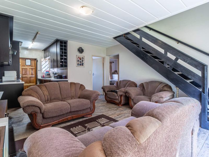 Open plan living area featuring laminate flooring, a staircase with a handrail, and an adjacent kitchen with built-in cabinetry.