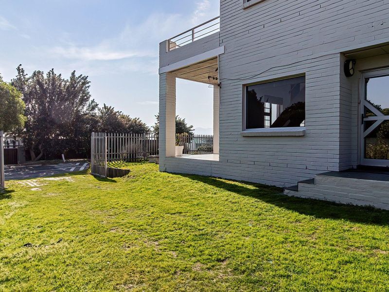 Rear view of a painted brick house featuring a covered patio, upper-level balcony with metal railing, and a well-maintained lawn area.