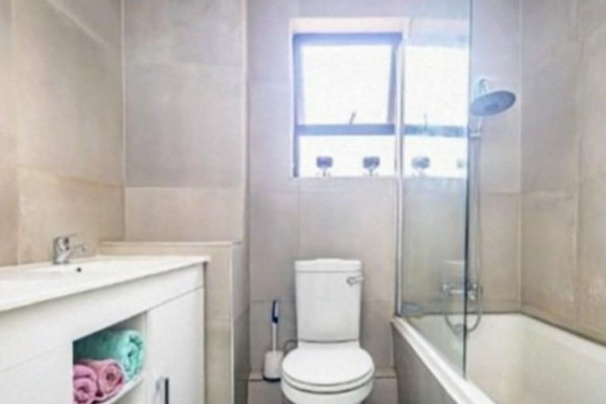 A modern bathroom featuring a vanity with integrated basin, a toilet, and a bathtub with a glass shower screen and tiled walls.