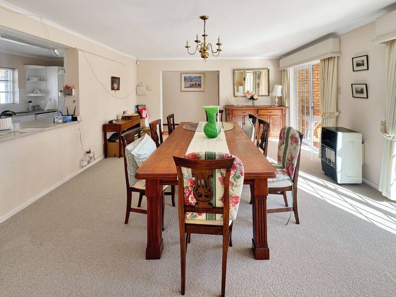 Spacious dining room featuring a classic chandelier, carpeted flooring, and a convenient pass-through window to the kitchen, with access to an outdoor area.