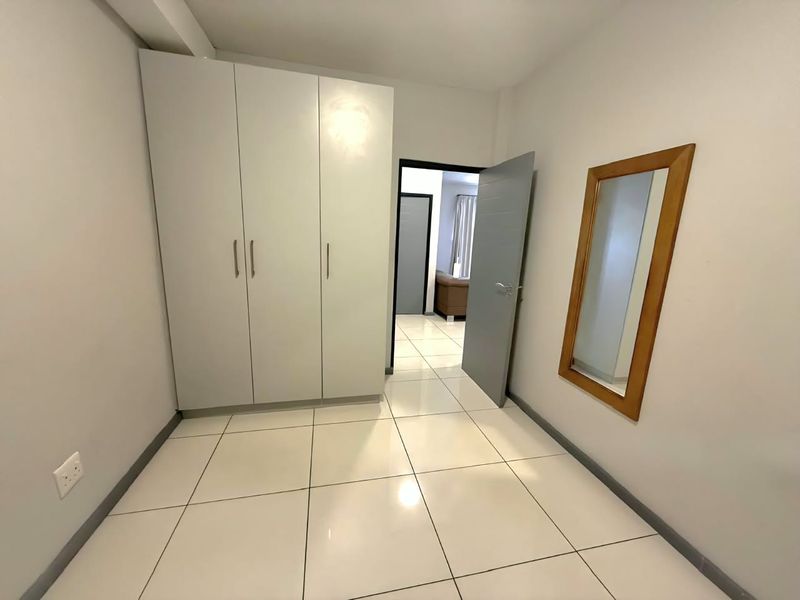 A clean and bright bedroom featuring neutral tiled flooring and a spacious built-in wardrobe, offering a versatile space ready for personalization.