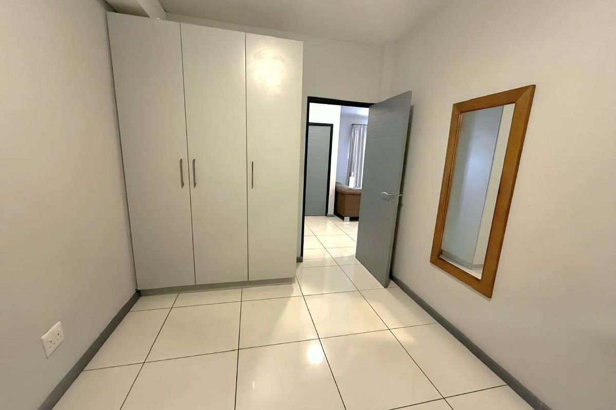 A clean and bright bedroom featuring neutral tiled flooring and a spacious built-in wardrobe, offering a versatile space ready for personalization.