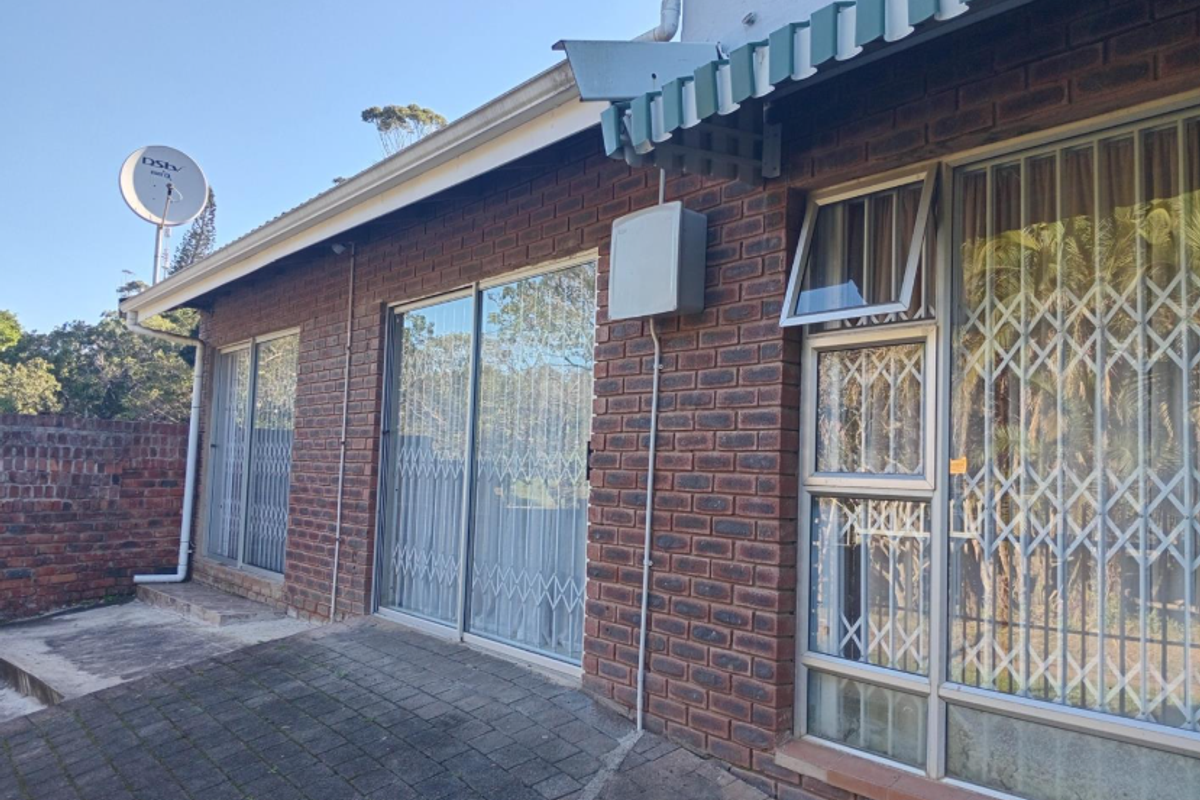 Exterior view of the rear facade featuring face-brick walls, sliding glass doors with security gates, and a paved patio area.