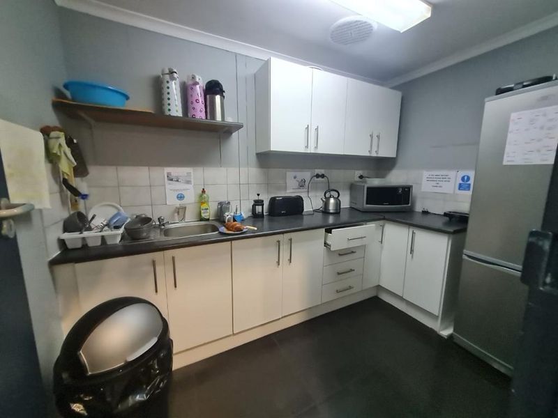 A functional office kitchenette featuring white cabinetry, dark laminate countertops, a stainless steel sink, and a tiled backsplash.
