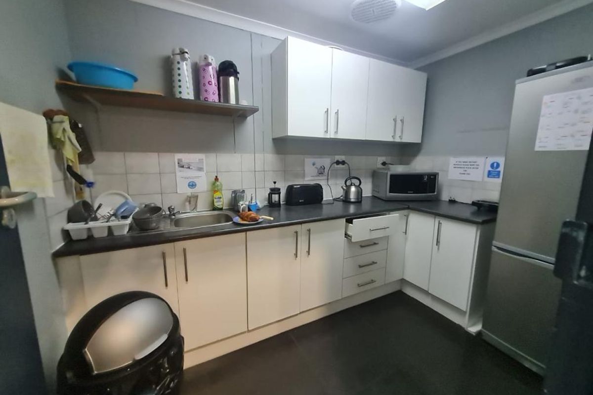 A functional office kitchenette featuring white cabinetry, dark laminate countertops, a stainless steel sink, and a tiled backsplash.