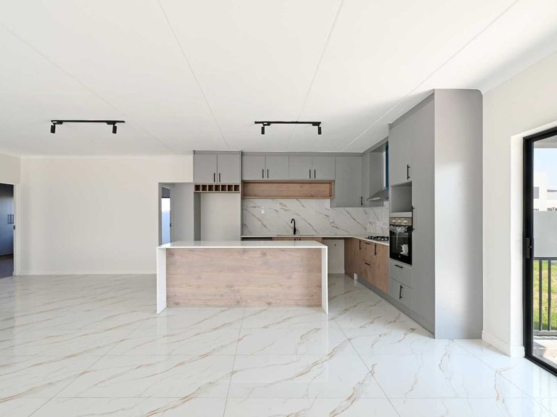 Modern open-plan kitchen featuring sleek grey and wood-tone cabinetry, marble-look tiled flooring, built-in appliances, and direct access to an outdoor balcony area.