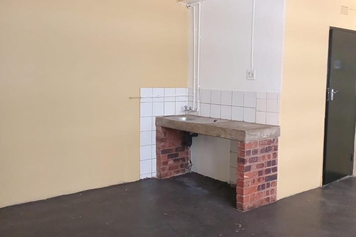A basic, empty kitchen area featuring a simple brick-based sink counter with tiled splashback and exposed plumbing, suitable for renovation.