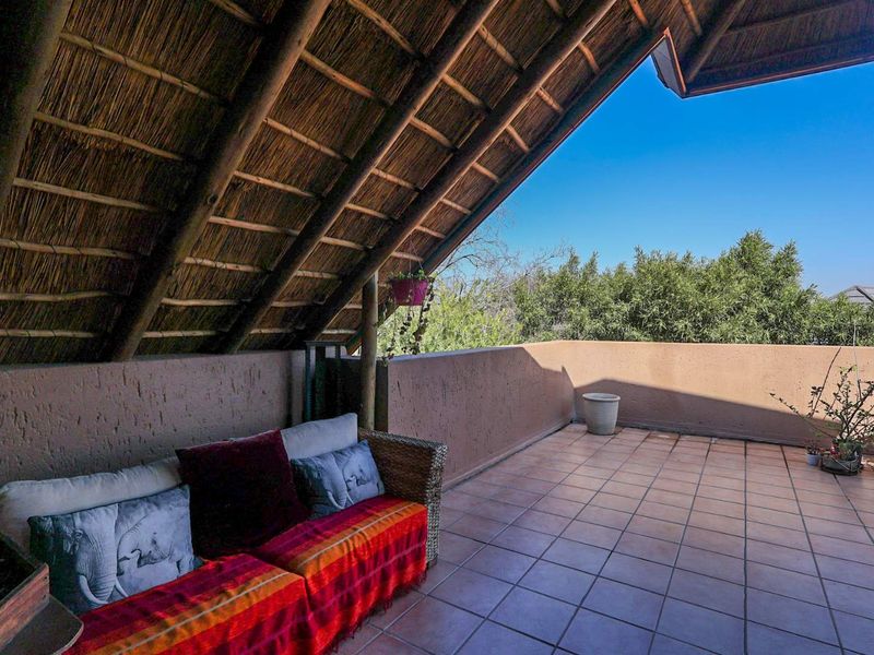 A spacious covered balcony featuring a traditional thatched roof, tiled flooring, and a masonry parapet wall, offering an open-air outdoor living space.