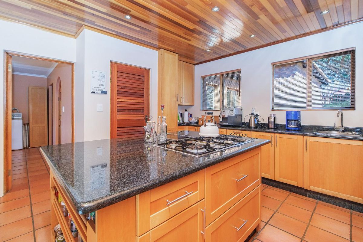 A functional kitchen featuring wooden cabinetry, granite countertops, a central island with a gas hob, and a distinctive timber-paneled ceiling.