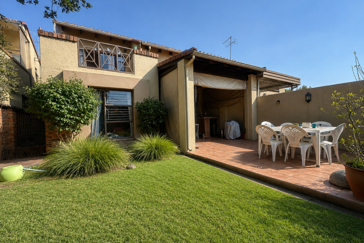 Rear view of the townhouse featuring a covered tiled patio, a private garden with lawn, and secure window treatments.