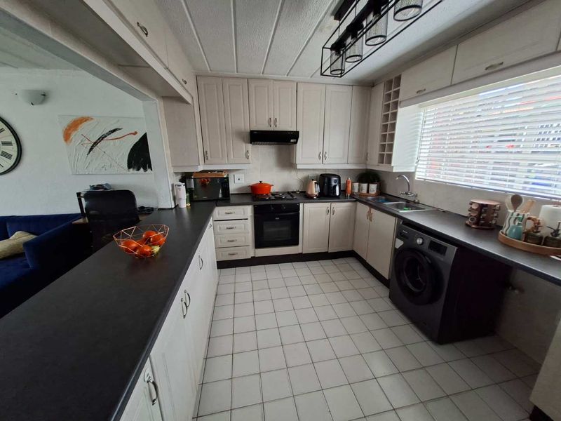 A functional kitchen featuring built-in cabinetry, dark laminate countertops, integrated oven and hob, and tiled flooring, with an open-plan layout connecting to the living area.