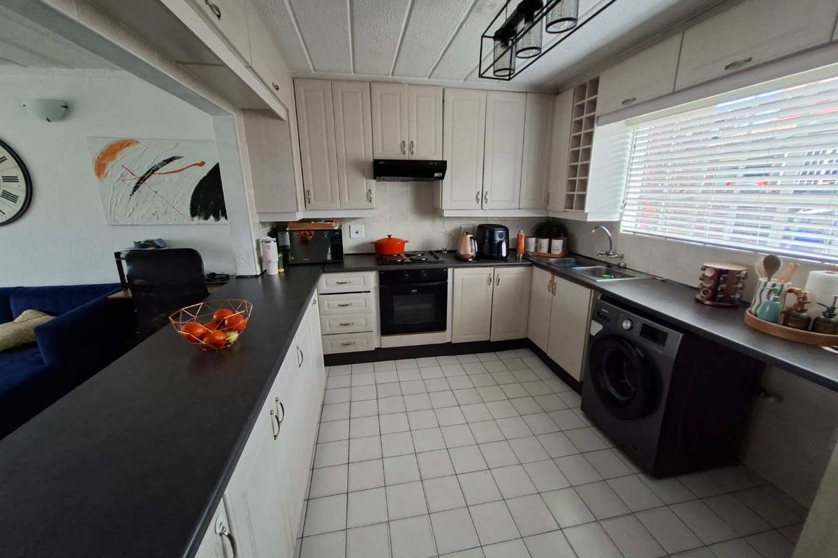 A functional kitchen featuring built-in cabinetry, dark laminate countertops, integrated oven and hob, and tiled flooring, with an open-plan layout connecting to the living area.