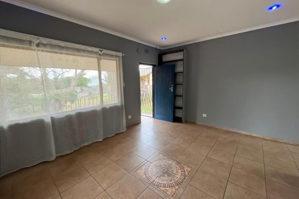 An empty living area featuring tiled flooring with a decorative inlay, recessed lighting, and a built-in shelving unit, leading to an exterior security gate.