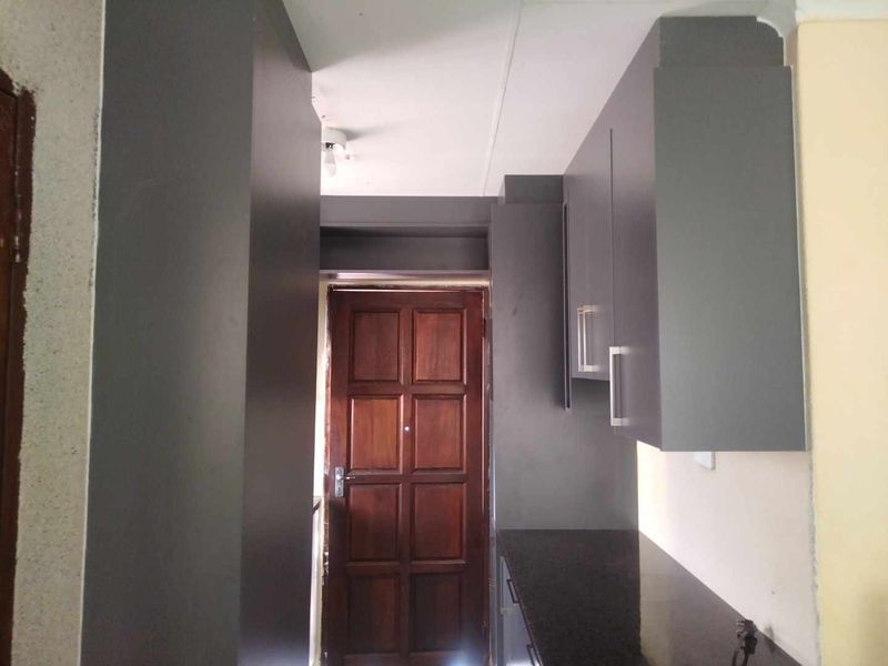 A compact kitchen area featuring dark grey built-in cabinetry, granite countertops, and a traditional solid wood door.