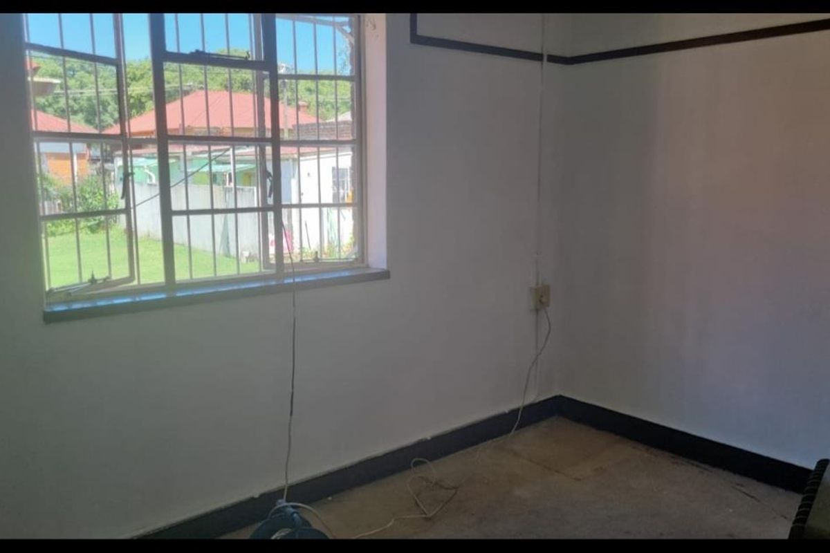 A vacant bedroom featuring a large window with security bars, neutral walls, and worn flooring, offering a blank canvas for renovation.