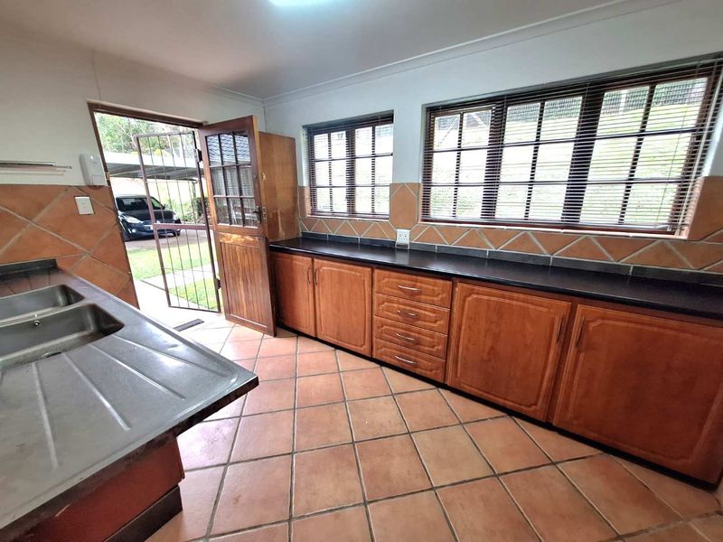 A functional kitchen featuring wooden cabinetry, black countertops, double stainless steel sink, and tiled flooring with direct access to the exterior.
