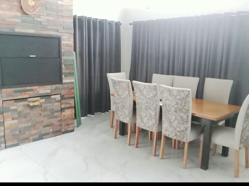 Dining area featuring a prominent stone-clad built-in fireplace, large format floor tiles, and neutral wall finishes.