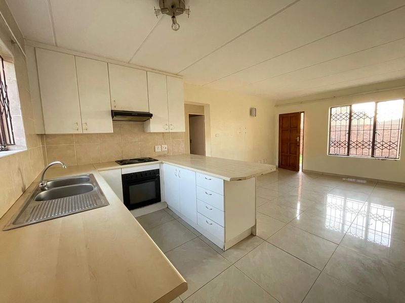 Open-plan kitchen and living area featuring tiled flooring, built-in cabinetry, and integrated appliances, offering a functional and bright living space.